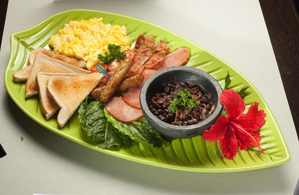 Tropical breakfast platter with scrambled eggs, bacon, toast and hibiscus flower